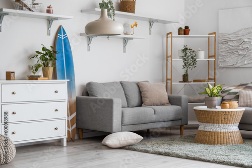 Interior of light living room with surfboard, commode and sofa