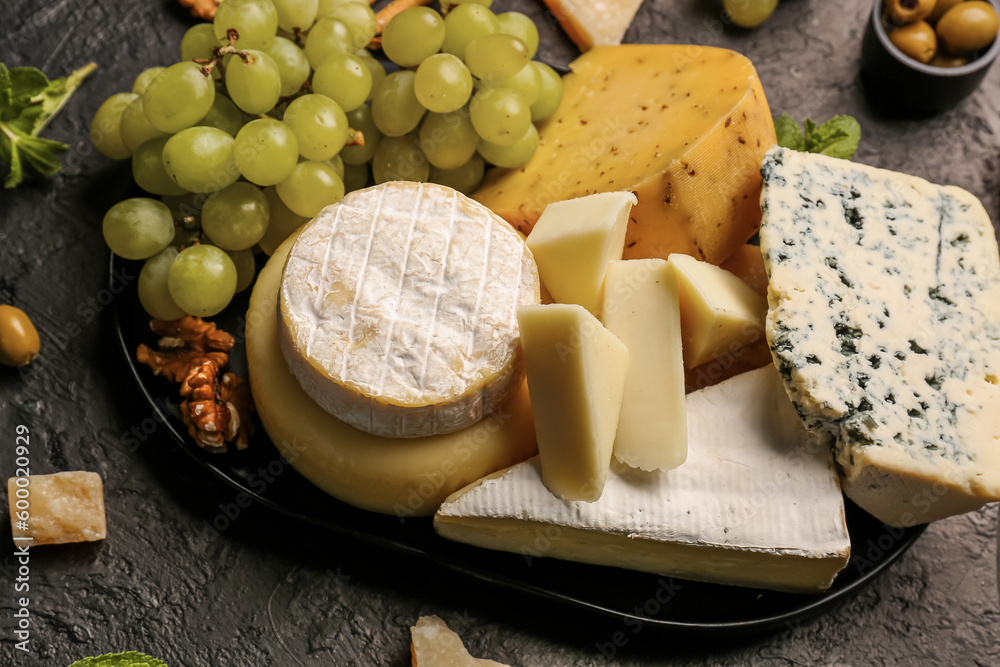 Tray with different types of tasty cheese and grapes on dark background
