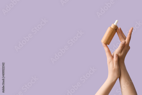 Hands holding bottle of essential oil on lilac background