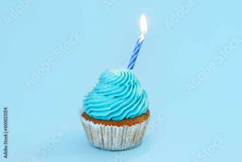 Tasty cupcake with birthday candle on blue background