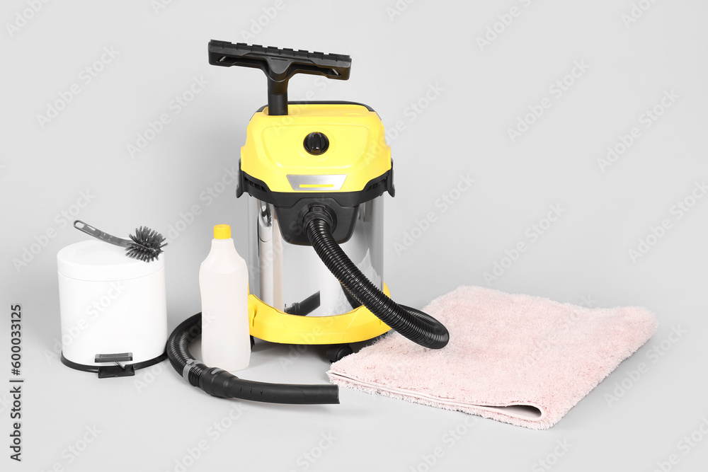 Naklejka premium Vacuum cleaner with supplies and carpet on grey background