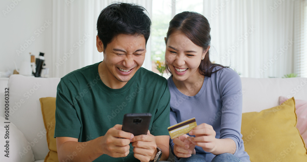 Secure pay gift card spend money buy ticket order from retail store on phone social media app. Asia people happy man woman, husband wife young couple sit at home sofa enjoy fun talk smile laugh relax.