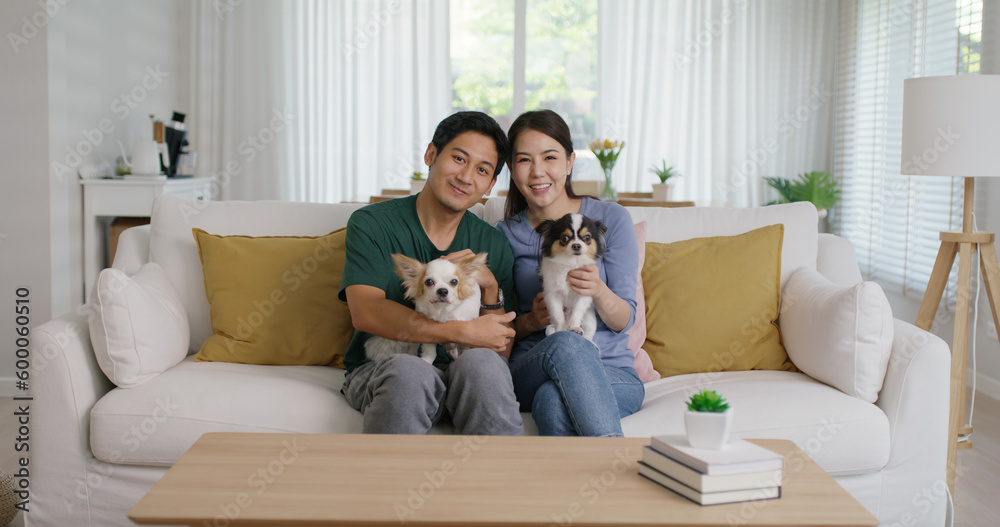Pet as baby child in Gen Z asia young adult couple hug cuddle dog sit at home sofa couch looking at camera. Selfie with small cute little chihuahua owner relax family cozy life love puppy animal lover - obrazy, fototapety, plakaty 