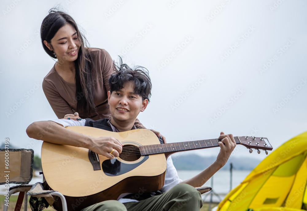 Wall Mural Young Asian couple play guitar and sing happily in nature on weekend