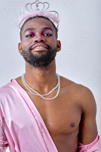 Male makeup look. Portrait of happy womanlike black man in pink shirt and crown, isolated over white studio background. young black american guy with necklace looking at camera. alone