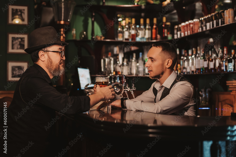 bartender at bar counter serves beer in glass to a male guest in pub
