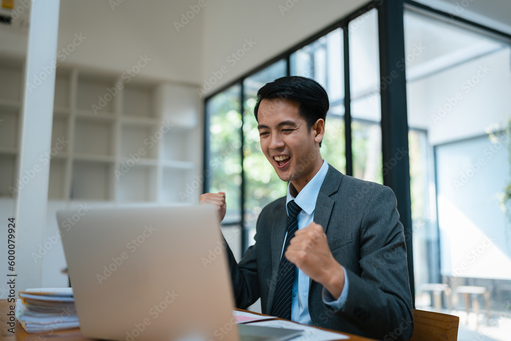 Portrait of an Asian male business owner standing with a computer showing happiness after a successful investment