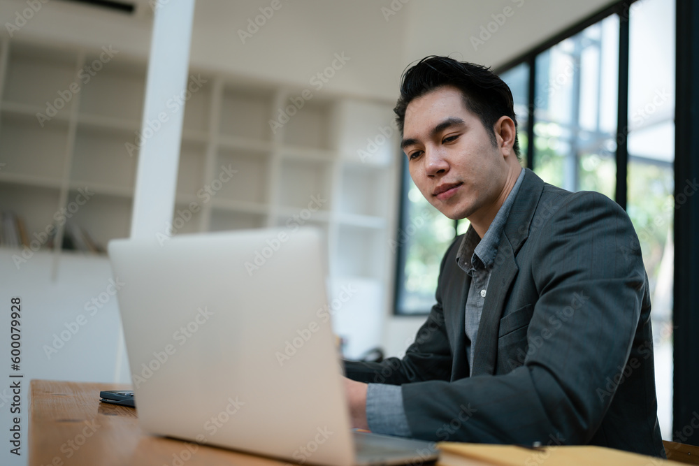 Portrait of an Asian male business owner standing with a computer showing happiness after a successful investment Portrait of an Asian male business owner standing with a computer showing happiness after a successful investment