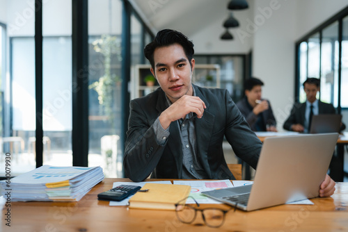 Portrait of an Asian male business owner standing with a computer showing happiness after a successful investment