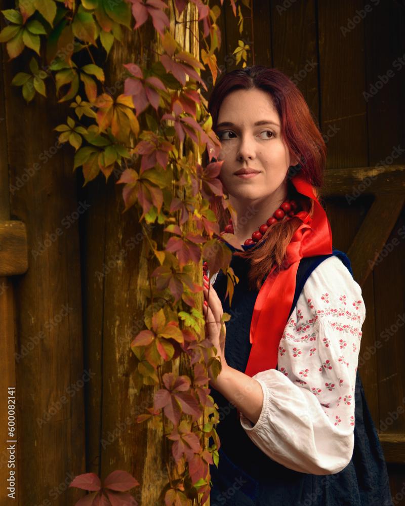 Smiling young redhead woman dressed traditional ukrainian embroidered clothes and red beads looking away. Vintage outfit. Half-length portrait.