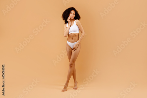 Body care concept. Slender black woman with perfect body shape posing on beige studio background, full length