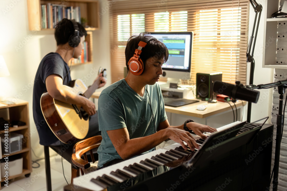 Group of Asian men making music at home studio. He plays guitar and keyboard.