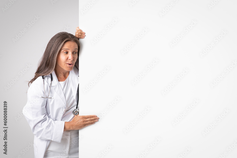 Promoting wellness. Surprised senior woman physician demonstrating empty placard board for medical advertisement, mockup