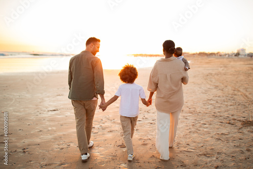 Young family taking a walk along the sea shore, holding hands with their child and walking on beach, back view © Prostock-studio