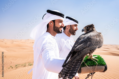 Two middle-eastern emirati men wearing arab kandura holding falcon in the desert