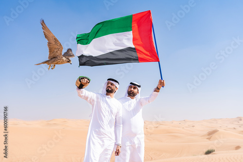 Two middle-eastern emirati men wearing arab kandura holding falcon in the desert photo