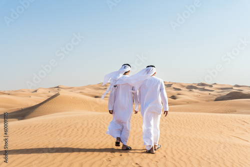 Two middle-eastern emirati men wearing arab kandura bonding in the desert