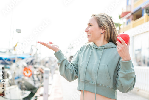 Young blonde woman with an apple at outdoors with surprise facial expression