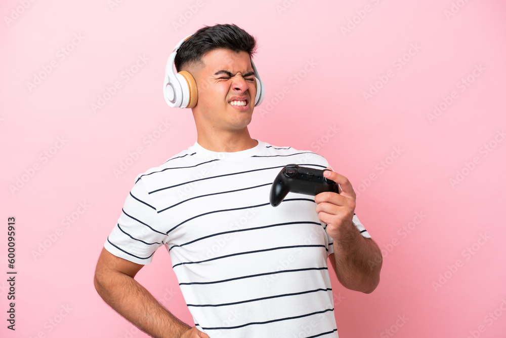 Young handsome man playing with a video game controller isolated on pink background suffering from backache for having made an effort Young handsome man playing with a video game controller isolated on pink background suffering from backache for having made an effort