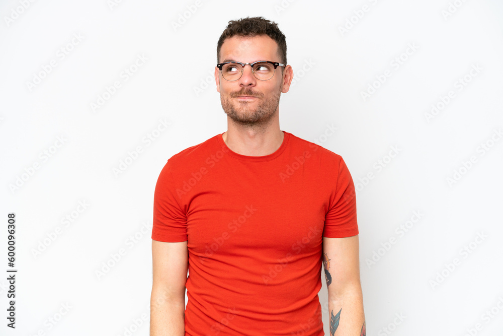 Obraz premium Young caucasian handsome man isolated on white background having doubts while looking up