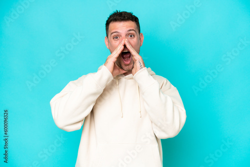 Young caucasian handsome man isolated on blue background shouting and announcing something