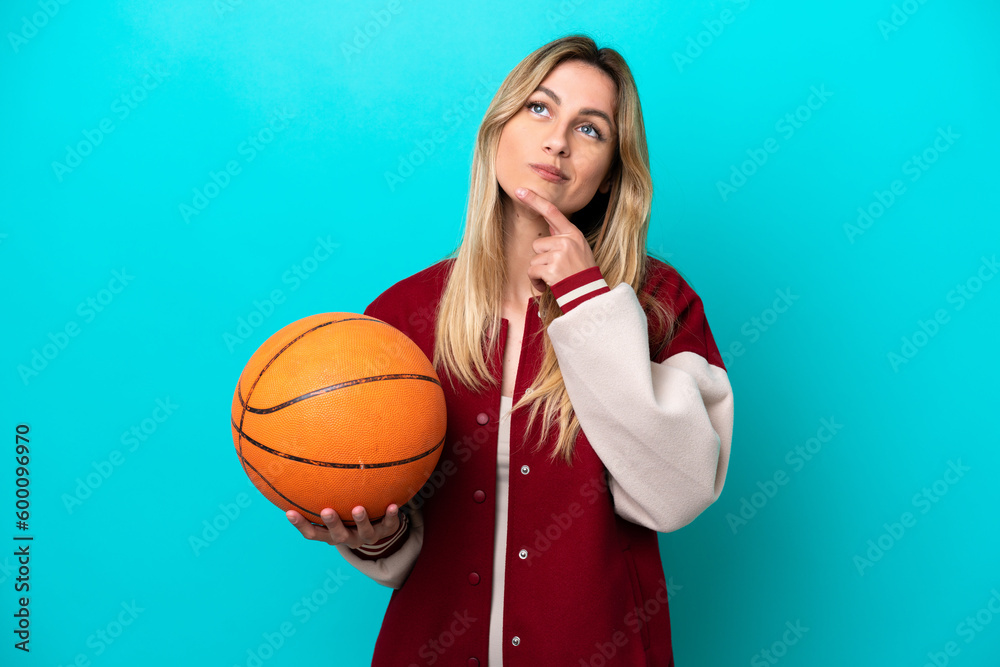 Young caucasian basketball player woman isolated on blue background having doubts while looking up