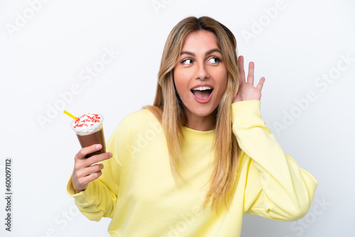 Young Uruguayan woman holding Frappuccino isolated on white background listening to something by putting hand on the ear