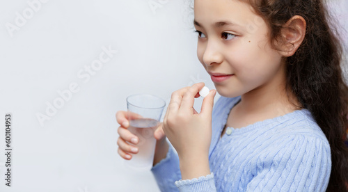 Half-breed child in blue sweater holds a magnesium or calcium tablet in his hand.