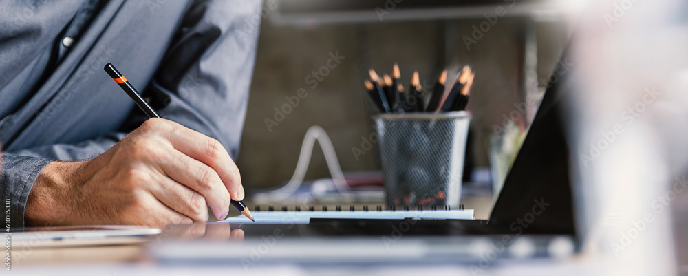 Close up man hand working of Architect sketching pencil project on blueprint at site construction work. Concept of architect, engineer in the office desk construction project banner