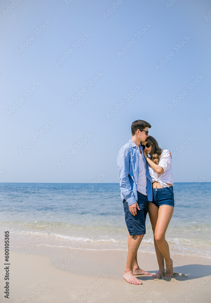 Portrait of beautiful caucasian woman with man wearing sunglasses walking on beach. Young couple enjoy honeymoon after marriage at sea. Happy casual lover hold at the tropical beach with copy space. Portrait of beautiful caucasian woman with man wearing sunglasses walking on beach. Young couple enjoy honeymoon after marriage at sea. Happy casual lover hold at the tropical beach with copy space.