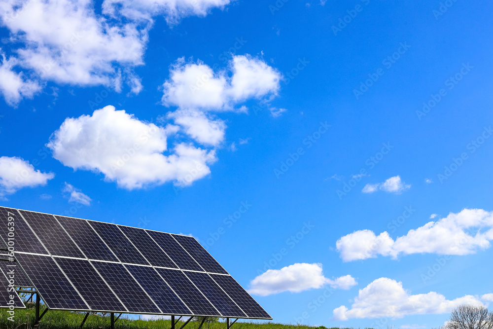 A working installation of solar batteries in the open air. Photoelectric batteries on the background of a saturated bright blue cloudy sky. Solar panels. Ecology, Concept of alternative energy A working installation of solar batteries in the open air. Photoelectric batteries on the background of a saturated bright blue cloudy sky. Solar panels. Ecology, Concept of alternative energy