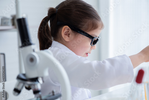 Cute little girl wearing lab coat learning chemistry in school laboratory  doing a chemical experiment while making analyzing and mixing liquid in glass at science class on the table.