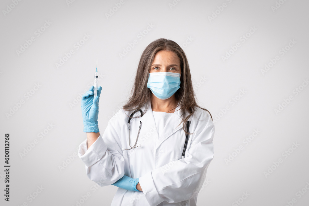 Immunization concept. Senior doctor woman in medical mask holding syringe with vaccine dose ready to make injection shot Immunization concept. Senior doctor woman in medical mask holding syringe with vaccine dose ready to make injection shot