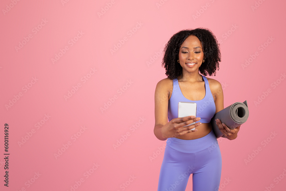 Cheerful millennial african american lady in sportswear with mat chatting on smartphone Cheerful millennial african american lady in sportswear with mat chatting on smartphone