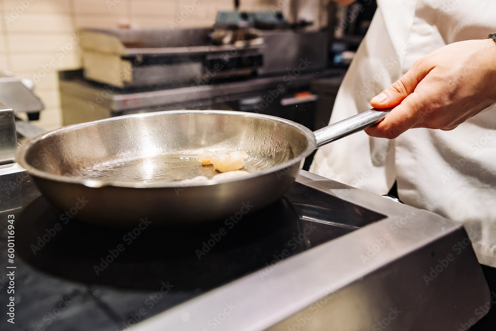 man chef cooking fried shrimp in frying pan on kitchen