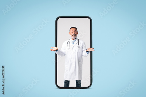 Positive european senior male doctor in white coat with stethoscope spreads arms to sides, holds free space