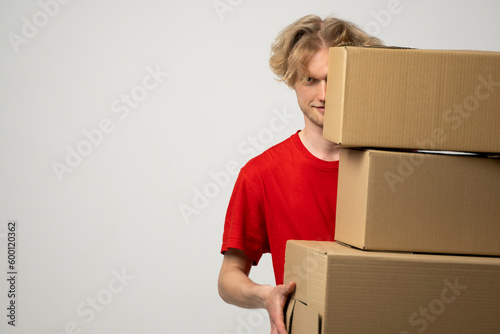 Courier in a red uniform holding a stack of cardboard boxes. Delivery man delivering postal packages over white studio background. © Volodymyr