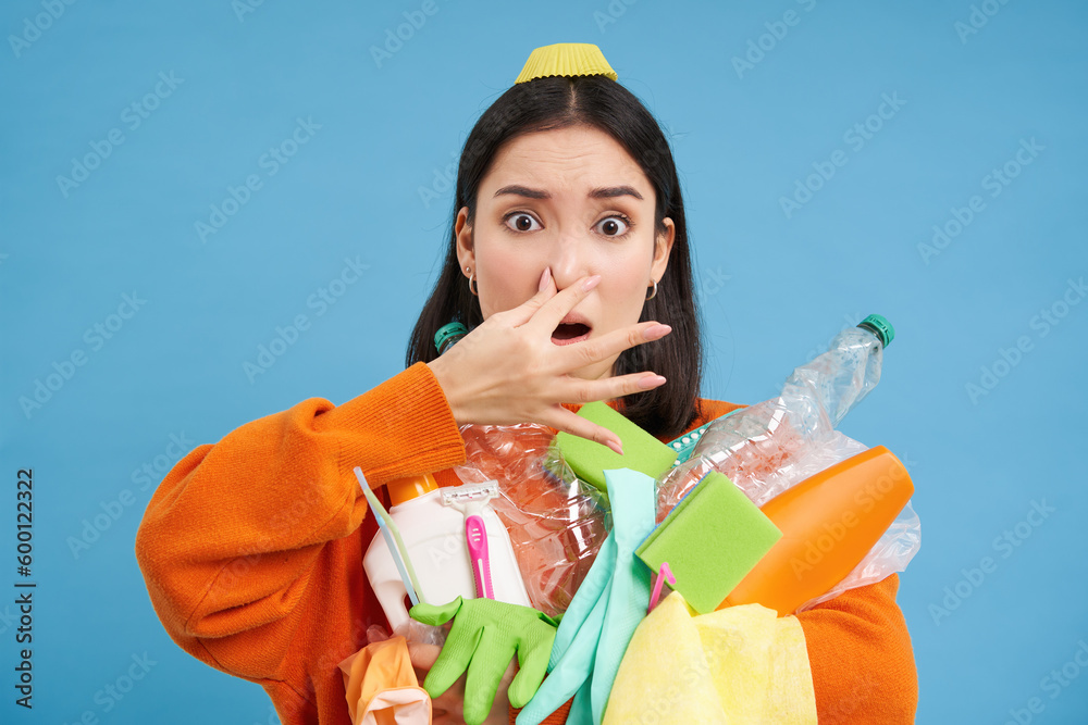 Portrait of woman shuts her nose from digust, holding stinky garbage