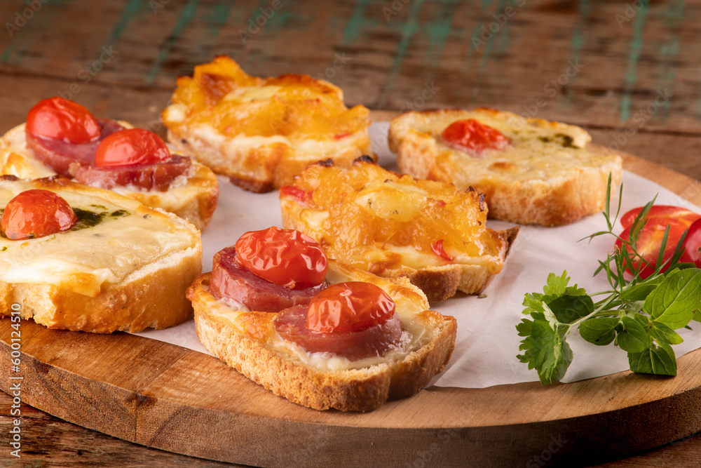 collection of bruschetta baked in slices of bread with melted cheese, cherry tomatoes on cattails on wooden table at an angle in close-up from the front