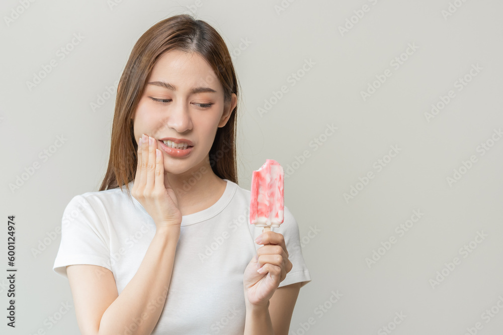 Face expression suffering from sensitive teeth and cold, asian young woman, girl hand touching her cheek, feeling hurt, pain eating ice cream, lolly. Toothache molar tooth at home, dental problem. Face expression suffering from sensitive teeth and cold, asian young woman, girl hand touching her cheek, feeling hurt, pain eating ice cream, lolly. Toothache molar tooth at home, dental problem.