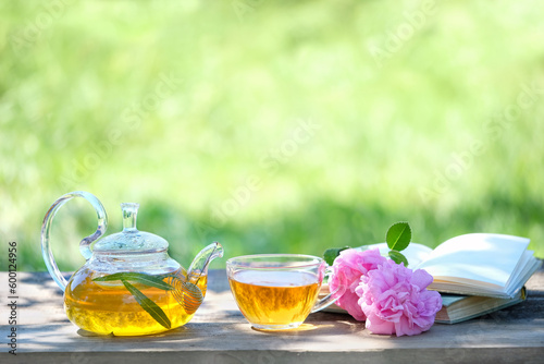 glass teapot and cup with herbal tea, flowers and book on table, natural abstract rustic background. summer season. relax time. useful calming tea. Tea party in garden. copy space