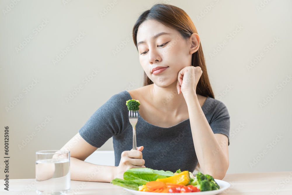 Diet in bored face, unhappy beautiful asian young woman, girl on dieting, holding fork in salad plate, dislike or tired with eat fresh vegetables. Nutrition of clean, healthy food good taste. Diet in bored face, unhappy beautiful asian young woman, girl on dieting, holding fork in salad plate, dislike or tired with eat fresh vegetables. Nutrition of clean, healthy food good taste.