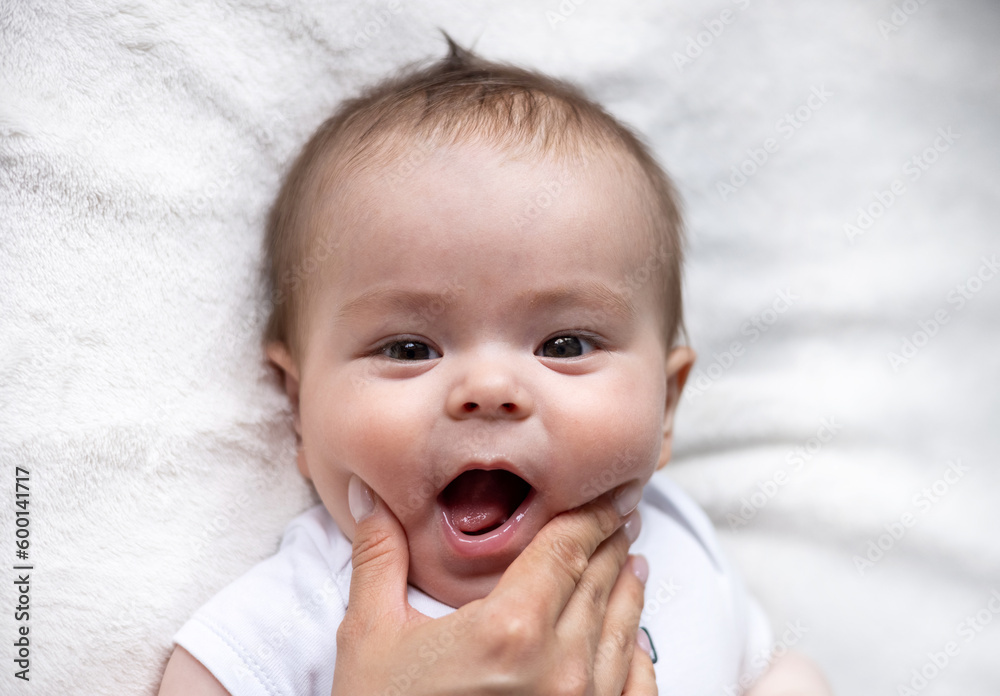 baby lying on bed holding feet with small hands, tongue out smiling profile side view.toddler infant playing with soft toy for teething.top view.adorable boy on bed.mother push checks with fingers baby lying on bed holding feet with small hands, tongue out smiling profile side view.toddler infant playing with soft toy for teething.top view.adorable boy on bed.mother push checks with fingers
