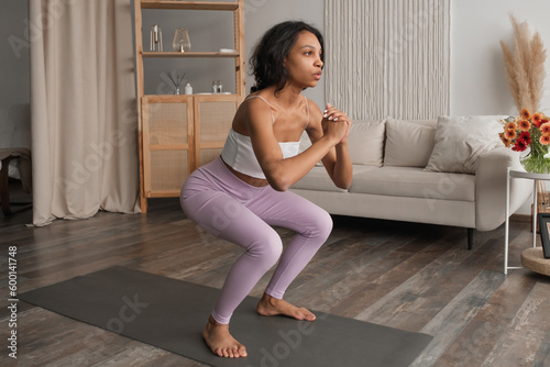 Side view on fit african woman doing squats at home.Healthy lifestyle. Wellness concept.Banner with copy space
