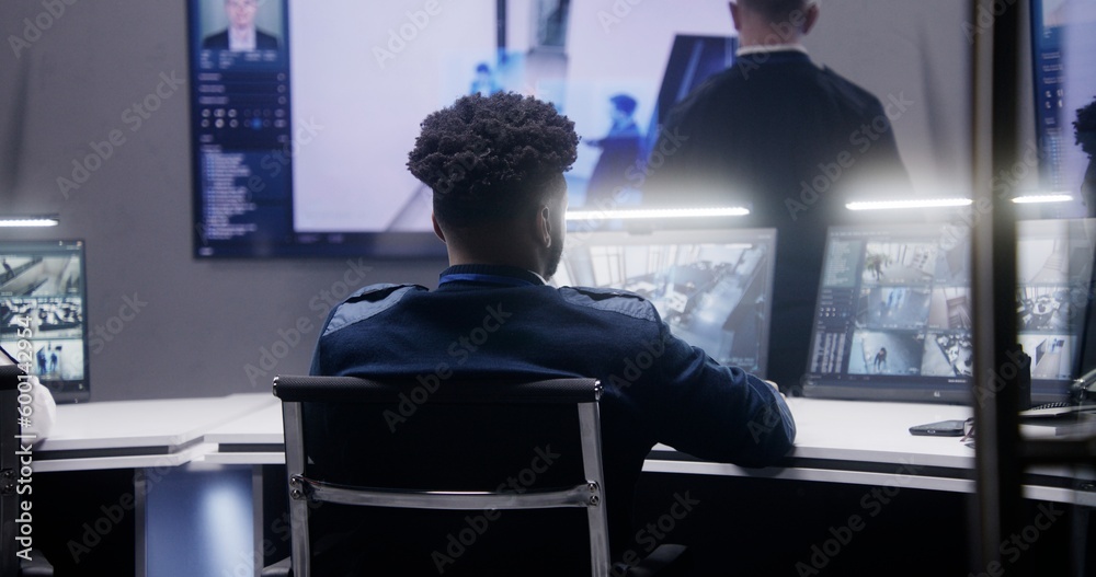 African American security operator monitors CCTV cameras with AI face