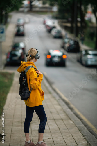 Woman view from behind wearing headphones and carrying a urban backpack on the streets of the city.