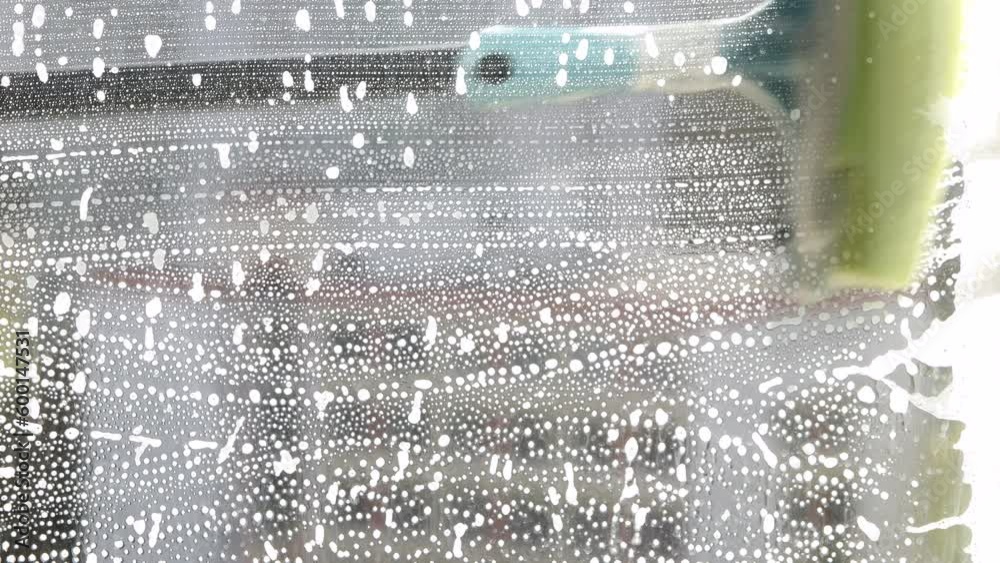 Someone is cleaning the house and washing the glass window with a brush with detergent and foam. Close-up.