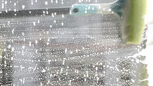 Someone is cleaning the house and washing the glass window with a brush with detergent and foam. Close-up.