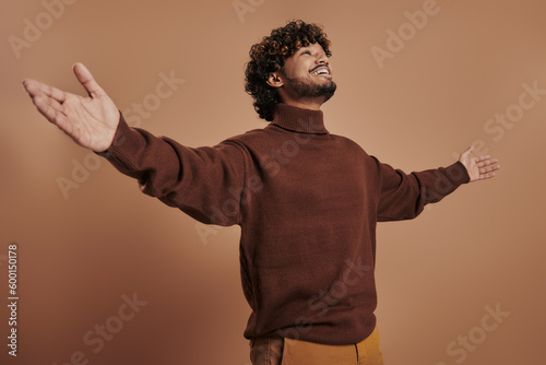 Relaxed Indian man stretching out hand and smiling against brown background