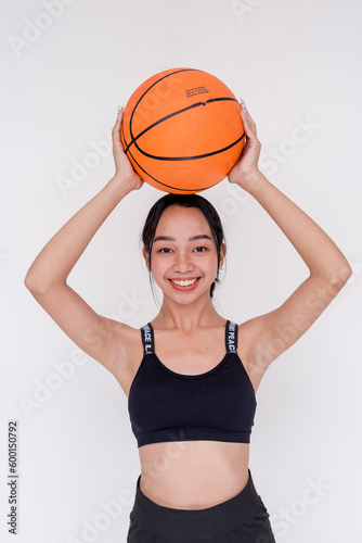 A sporty and athletic young woman posing while holding up a basketball above the head with both hands. Isolated on a white background.